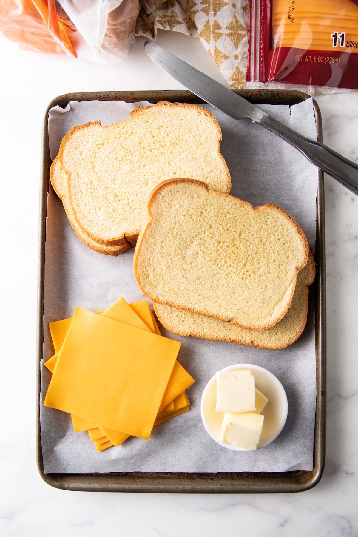 Ingredients on a small sheet tray to make grilled cheese sandwiches - sliced bread, cheddar cheese, and butter