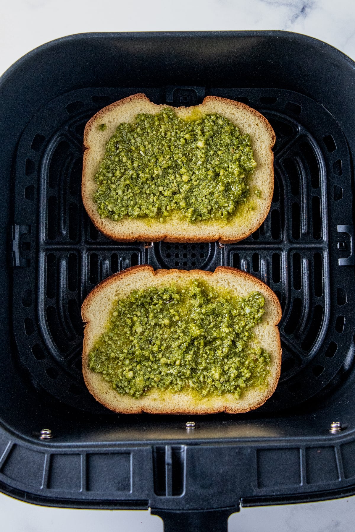 two slices of bread with pesto in an air fryer tray