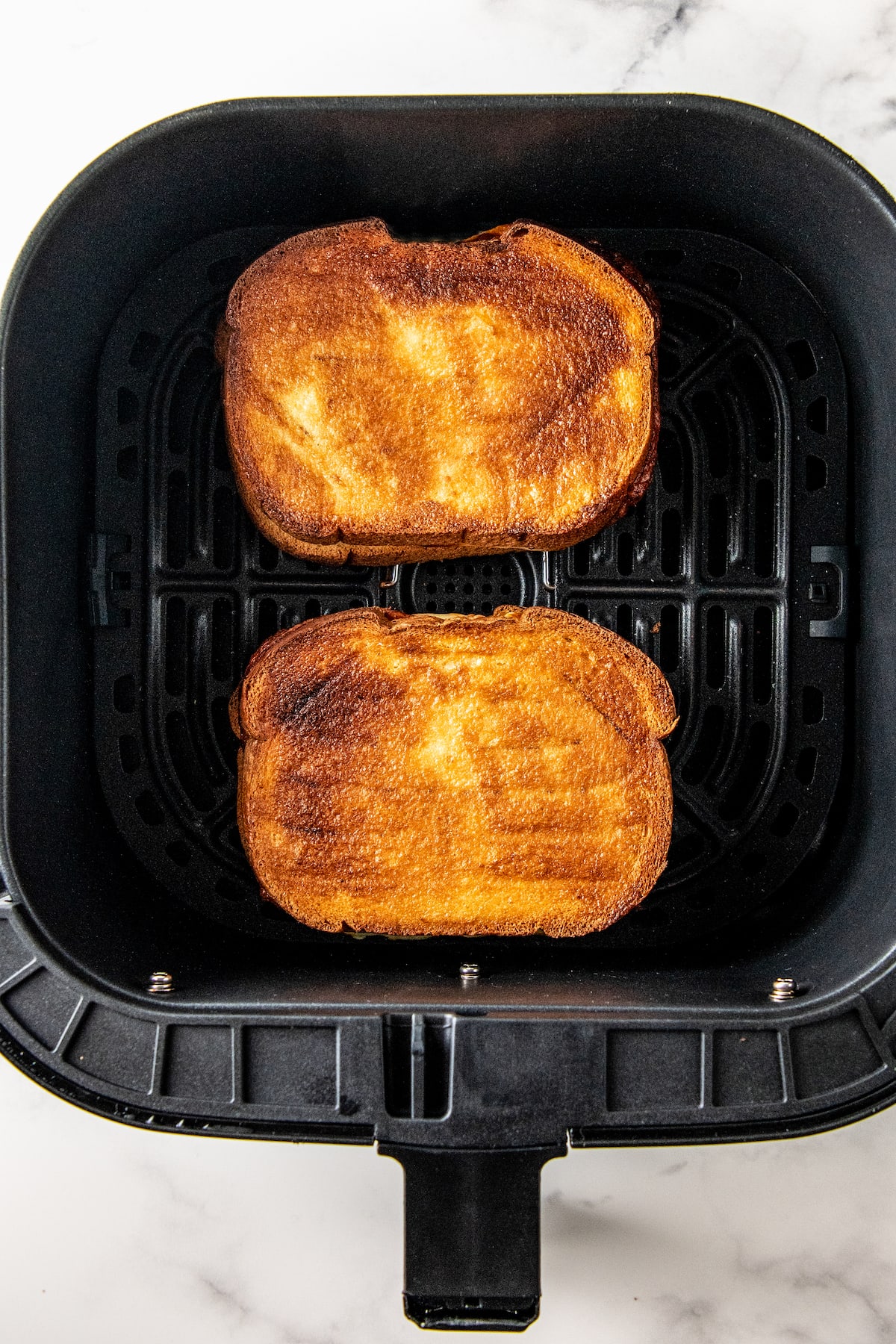 two toasted sandwiches in an air fryer tray