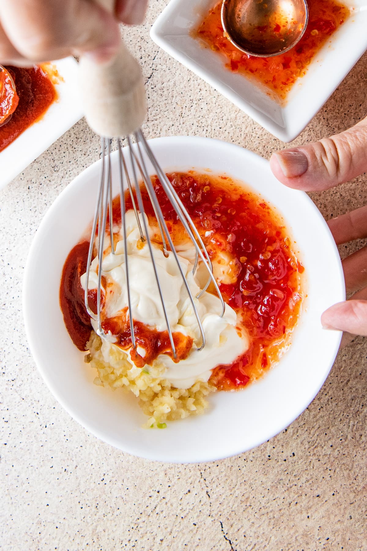 whisking together chili sauce, garlic, and sour cream to make bang bang sauce