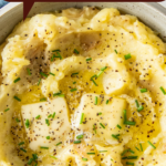 Mashed potatoes in a bowl with melted butter and chives on top.