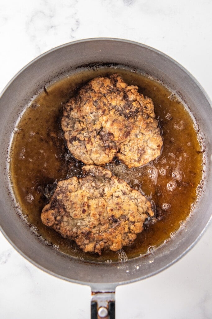 two cubed steaks frying a pan with hot oil