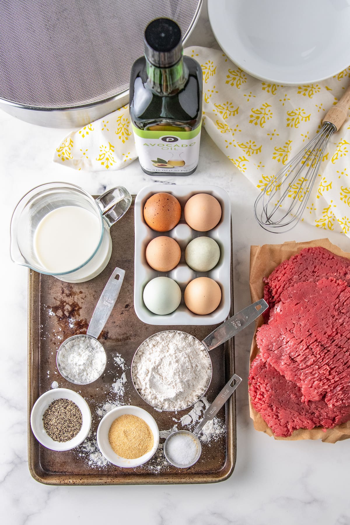 an assortment of ingredients to make chicken fried steak including cubed steak, eggs, flour, spices, and milk