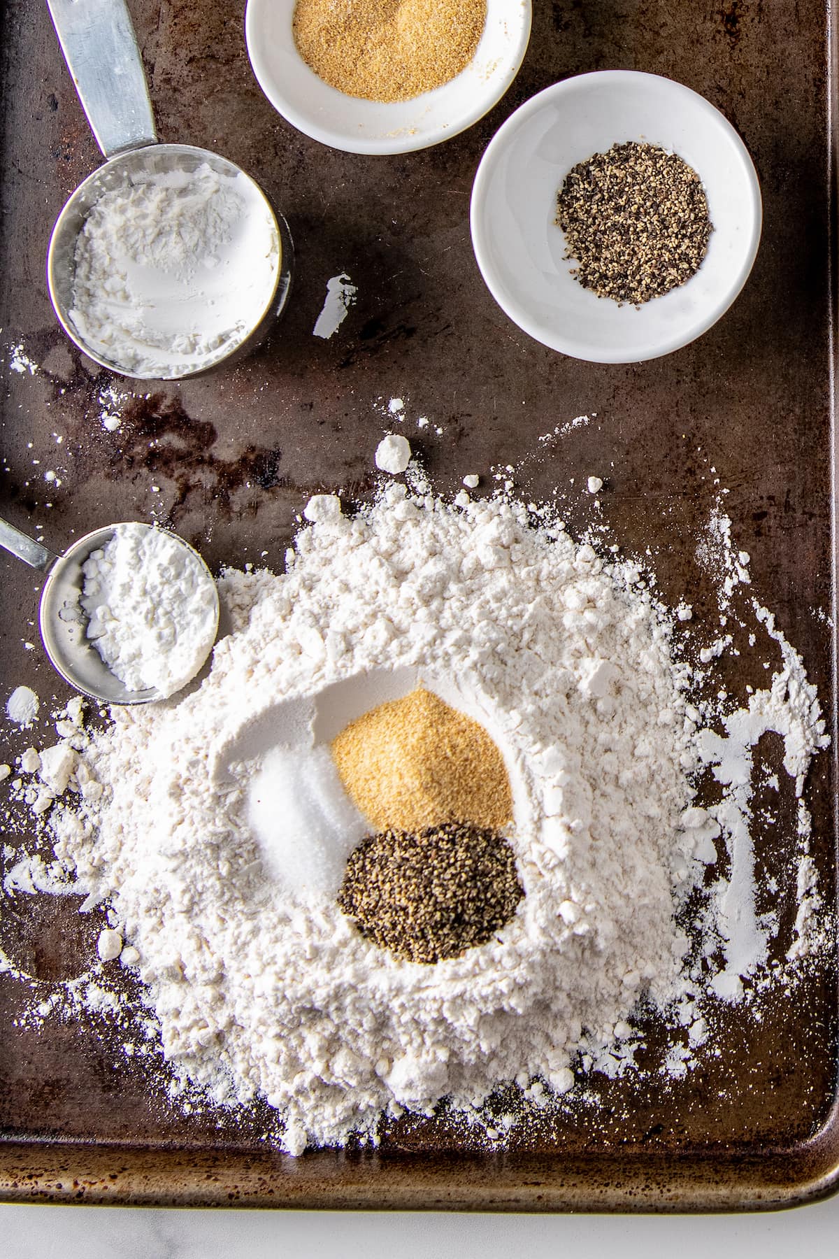 a pile of flour on a sheet tray with a well and assorted spices in the middle