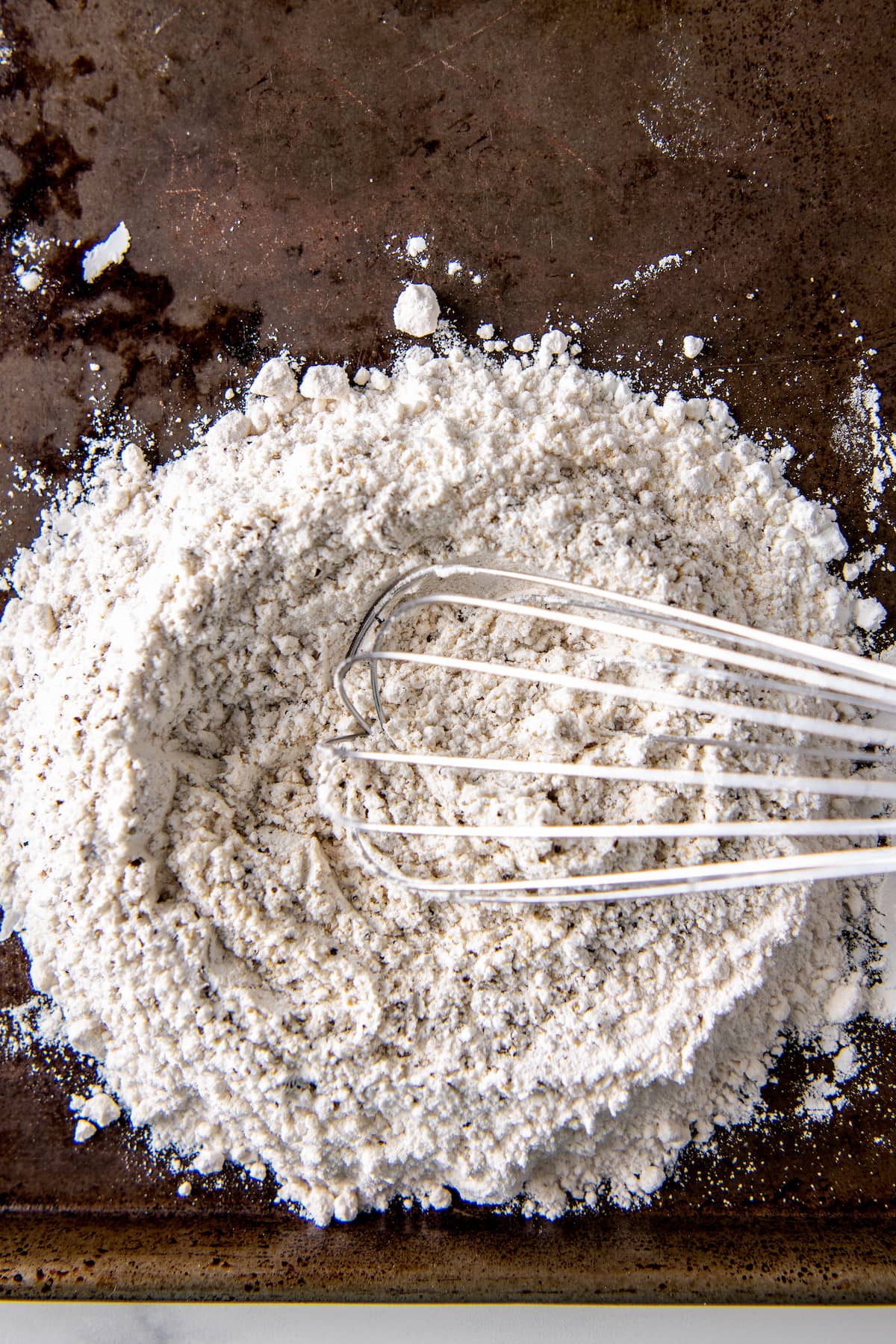 a whisk in a pile of flour on a sheet tray