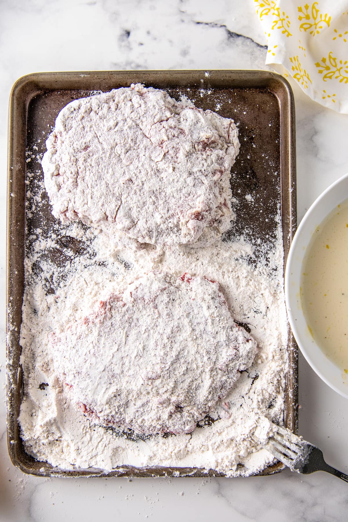 cubed steak dredged in flour on a sheet tray