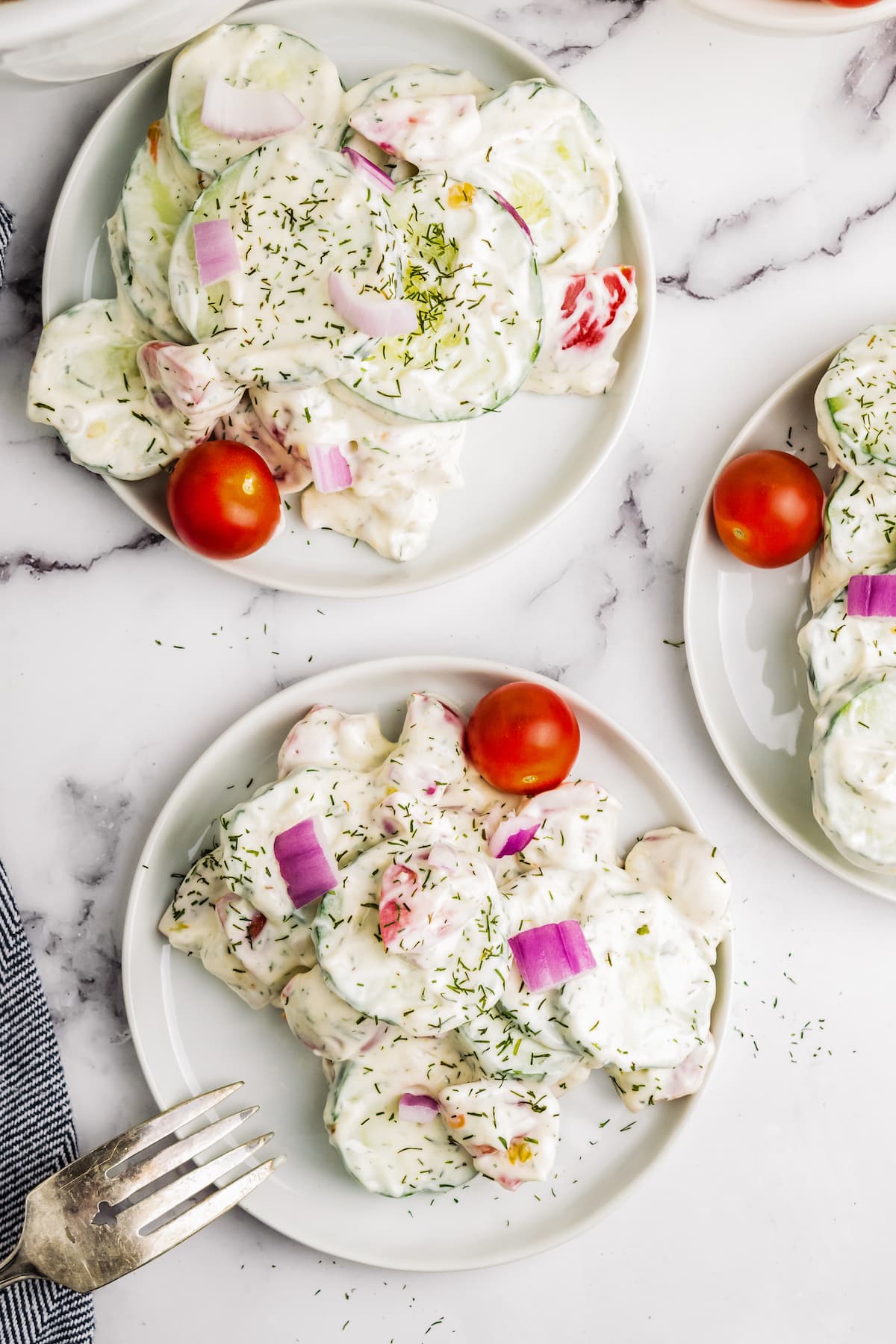 three plates with a creamy cucumber salad and cherry tomato for garnish