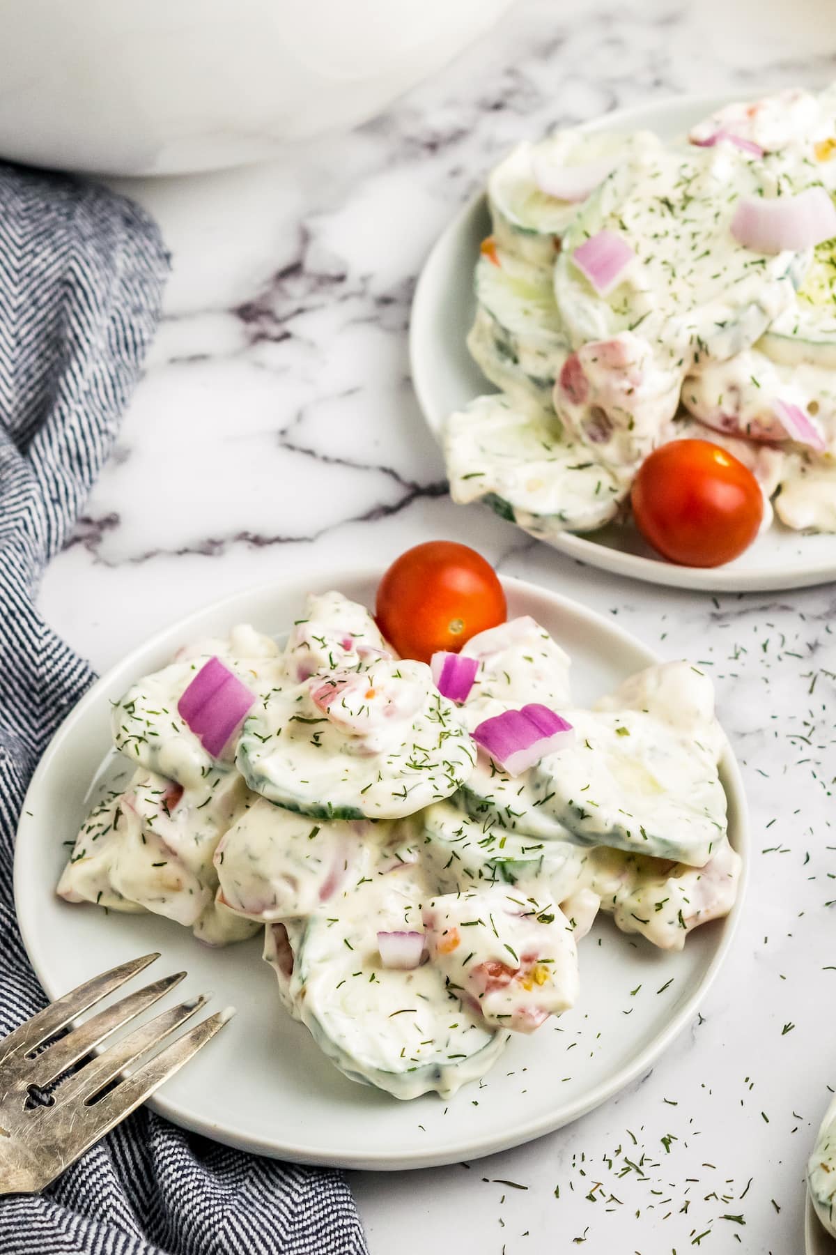 two plates with a creamy cucumber salad and cherry tomato for garnish