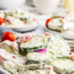 close up of creamy cucumber saald with red onions and tomato garnish