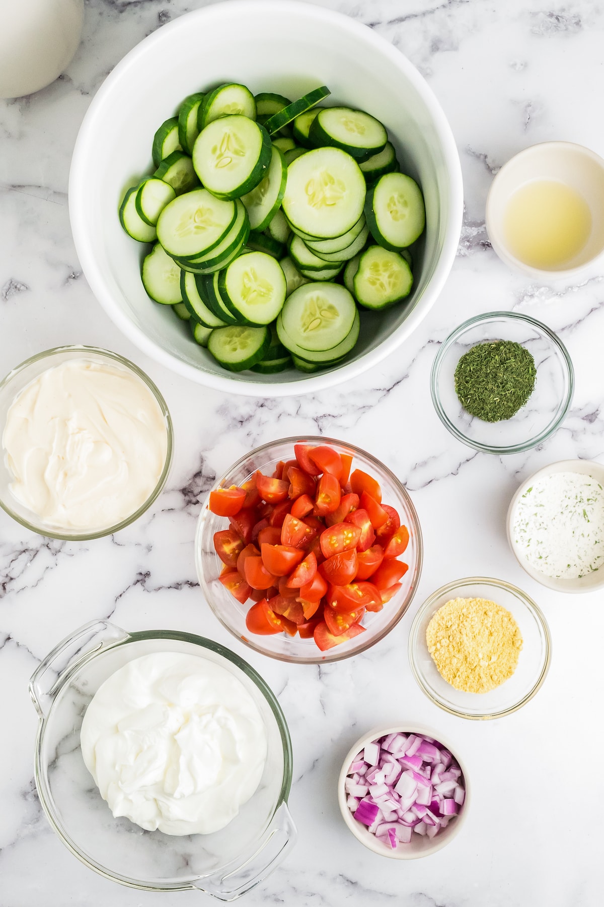 ingredients to make cucumber salad like a bowl of sliced cucumbers, tomatoes, seasonings, and dressing