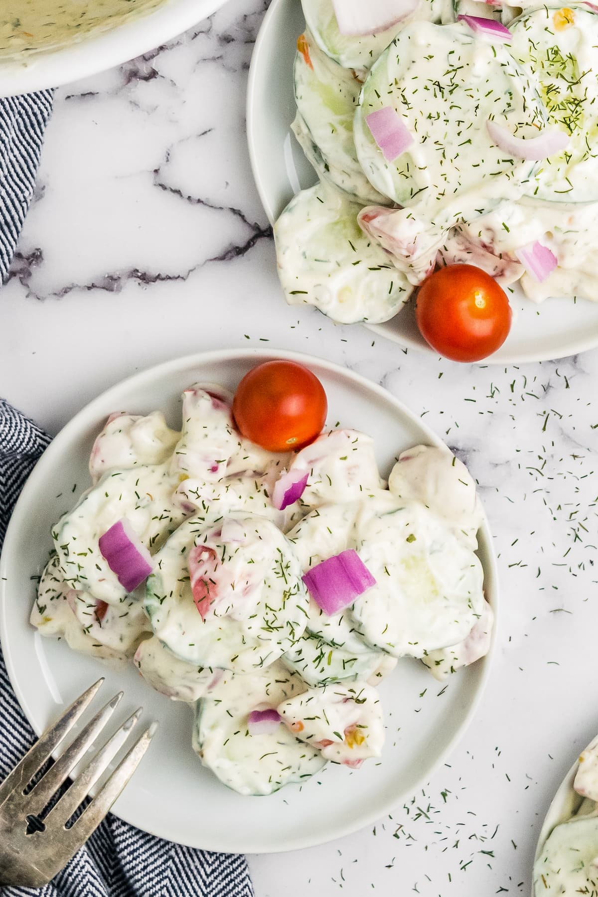 two plates with a creamy cucumber salad and cherry tomato for garnish