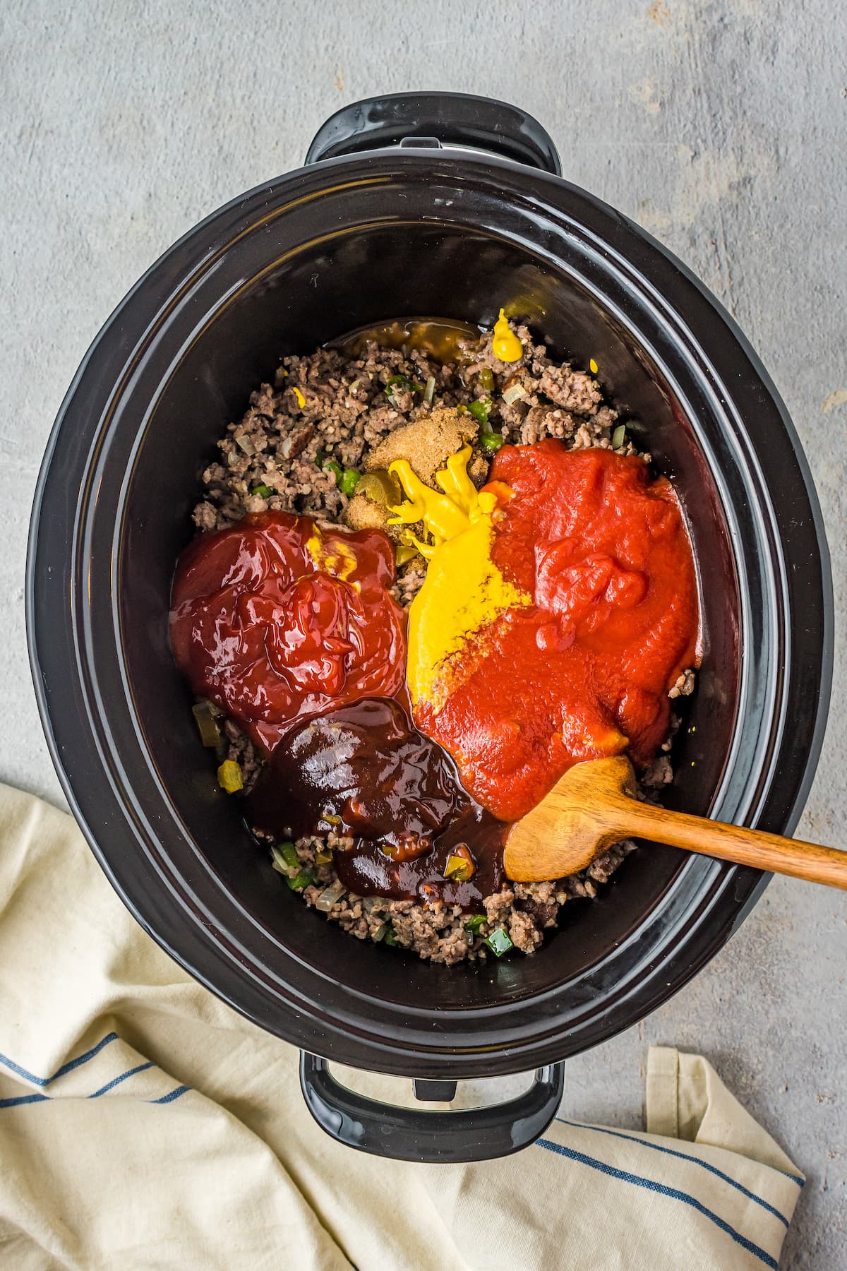 ground beef in a crock pot with ketchup, mustard, tomato sauce, and bbq sauce on top