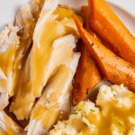 Crockpot turkey with gravy on a plate with mashed potatoes and carrots.