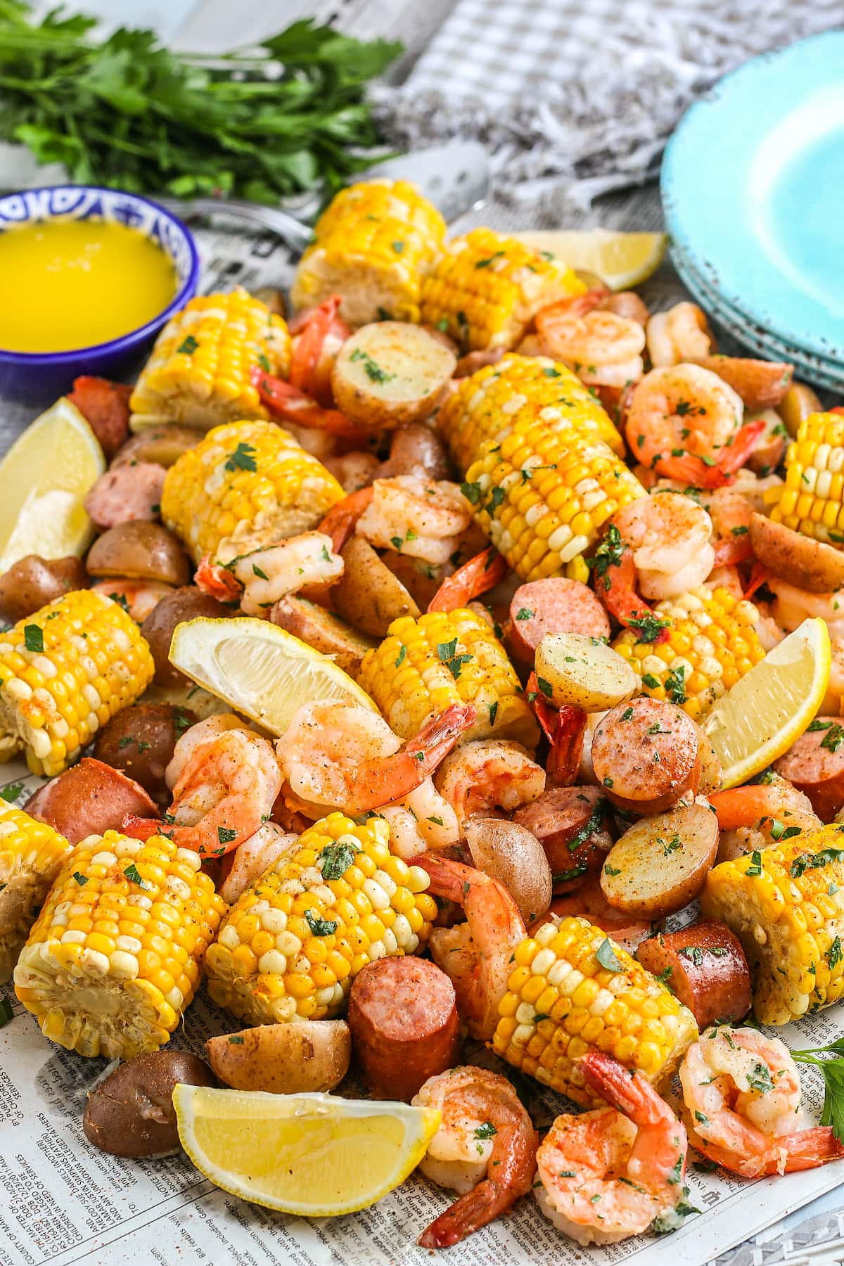 shrimp boil with shrimp, sausage, corn on the cob, lemons, and potatoes and a side of melted butter