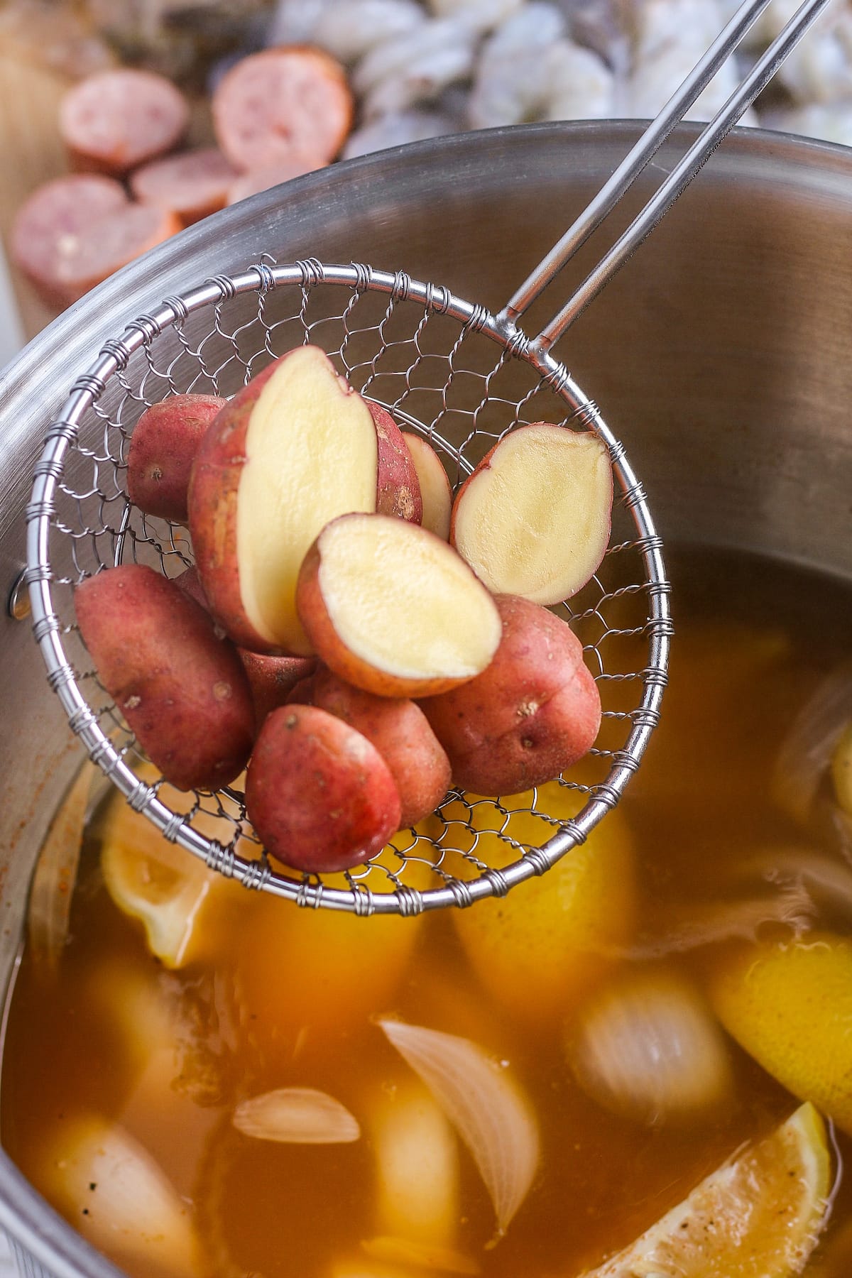 cut up potatoes over a pot with broth and cooked corn on the cob and other potatoes