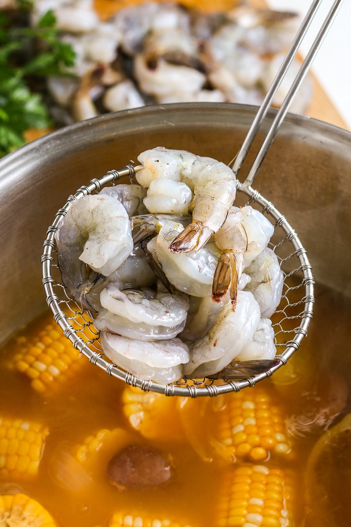 raw shrimp in a strainer spoon over a pot