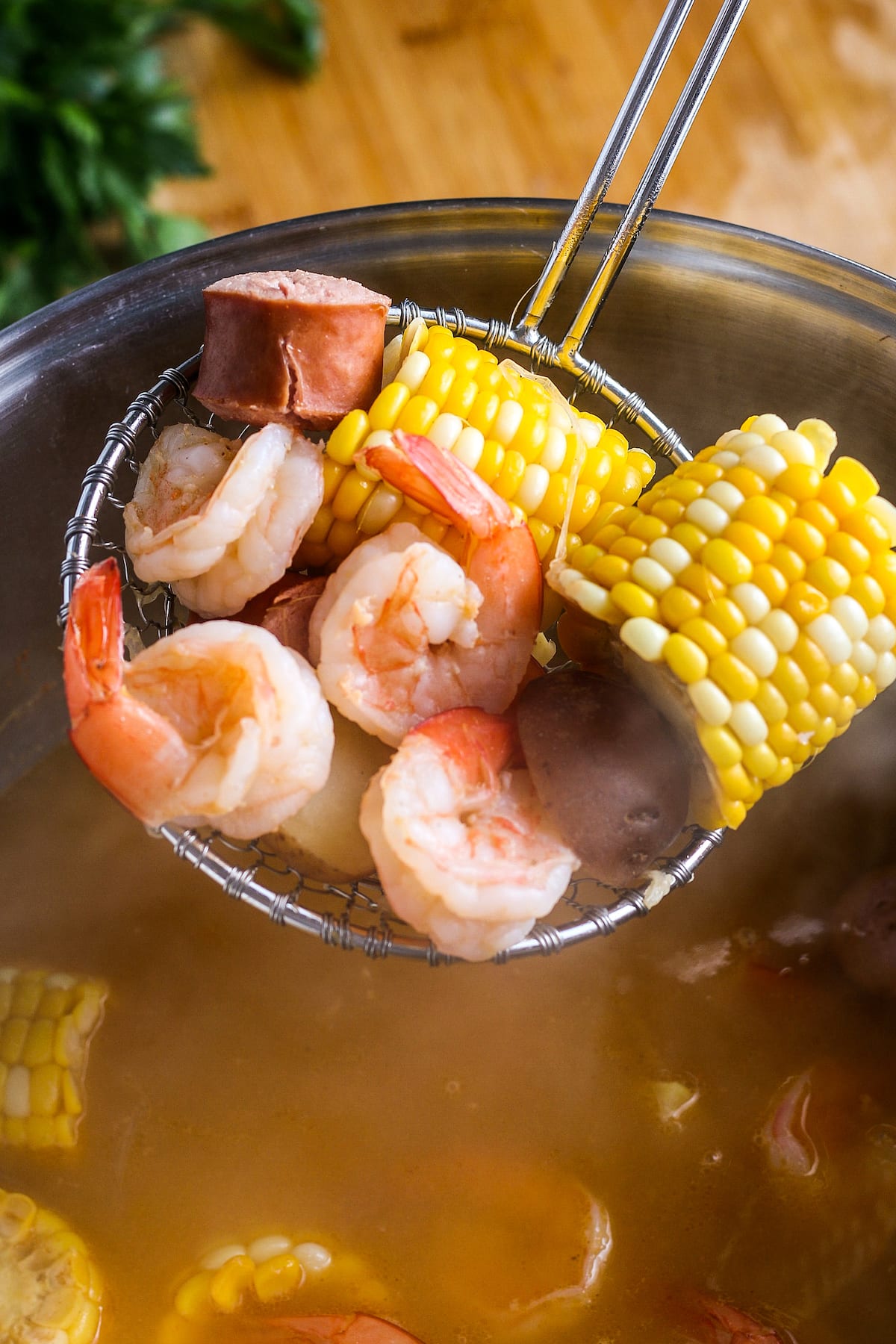 a ladle with cooked shrimp, sausage peices and corn on the cob