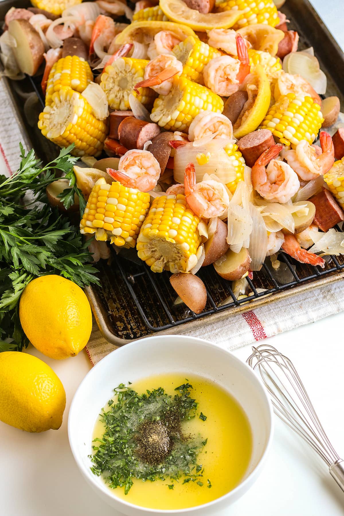 shrimp boil with shrimp, sausage, corn on the cob, lemons, and potatoes and a side of melted butter with herbs