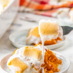 taking a bite out with a fork of a portion of sweet potato casserole with marshmallows on a plate