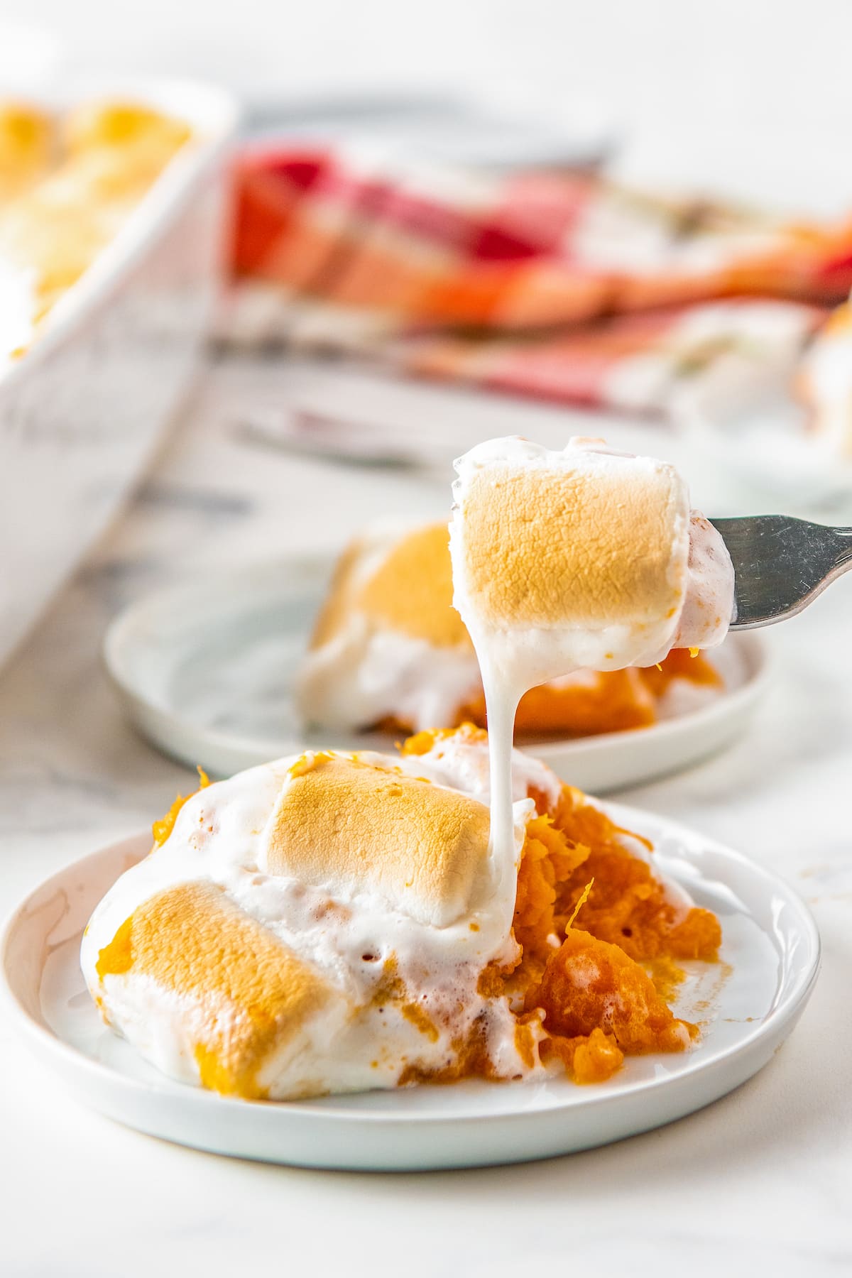 taking a bite out with a fork of a portion of sweet potato casserole with marshmallows on a plate