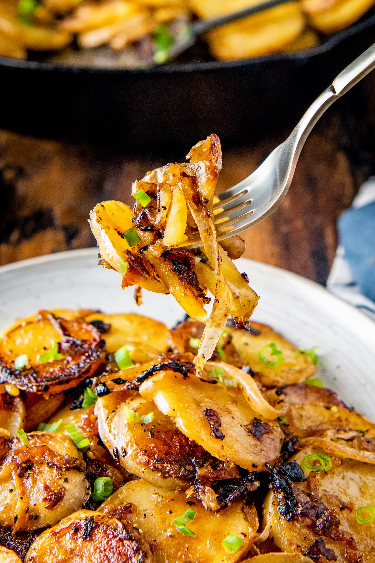 a plate of fried sliced potatoes and onions garnished with chives wih a fork taking out a bite