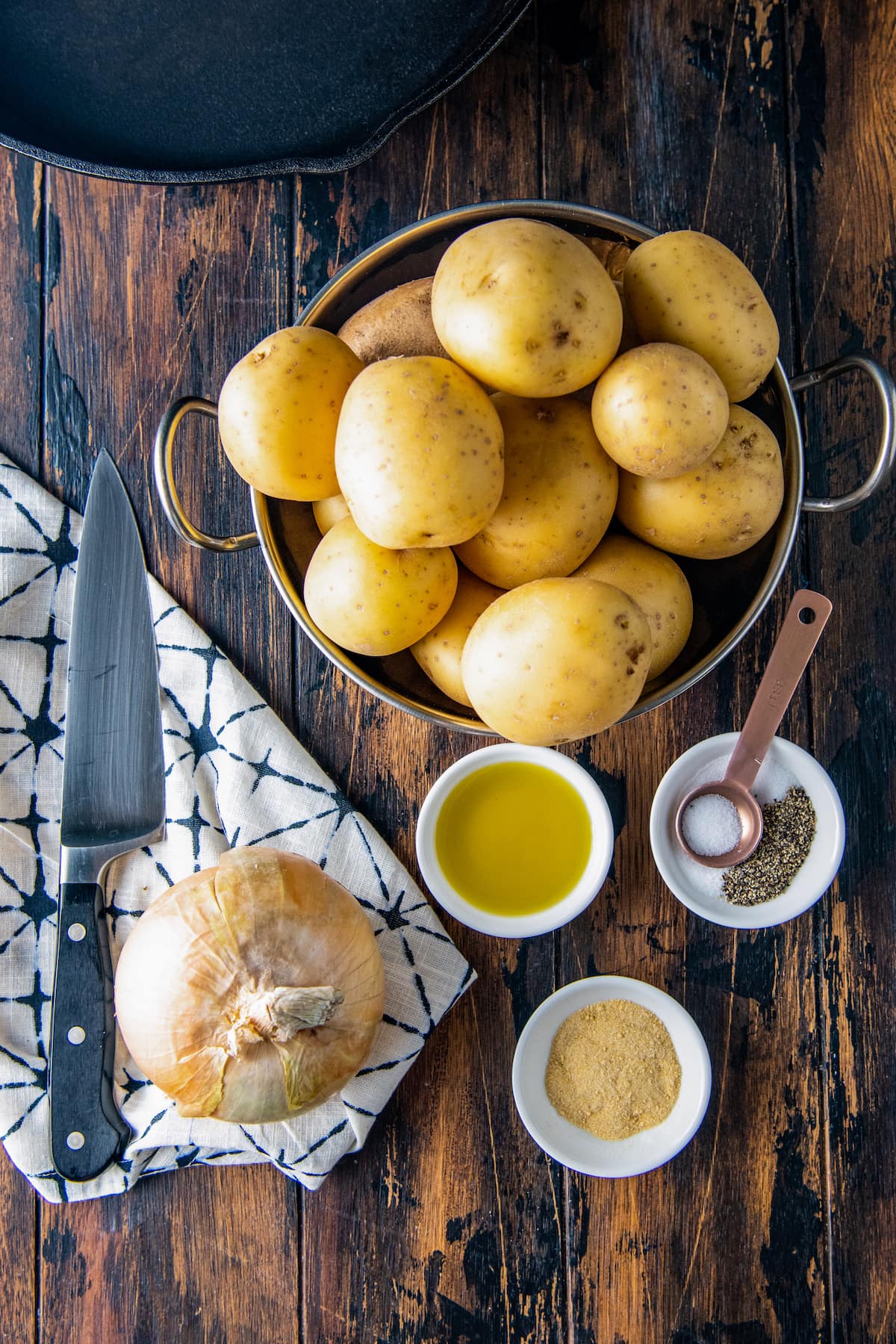 a bowl of potatoes alongside an onion, olive oil, garlic powder, salt and pepper