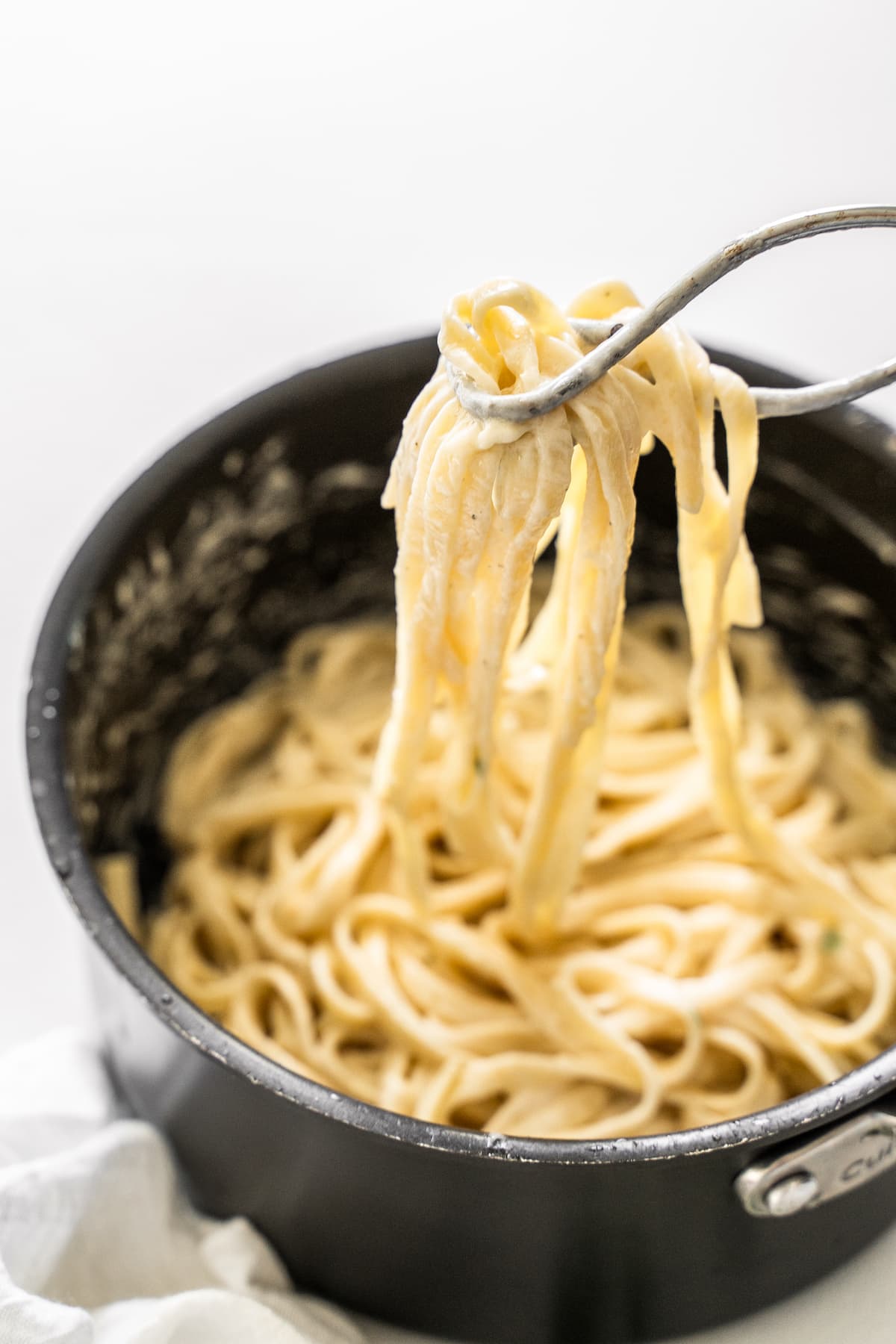 tongs lifting pasta in alfredo sauce out of a pot