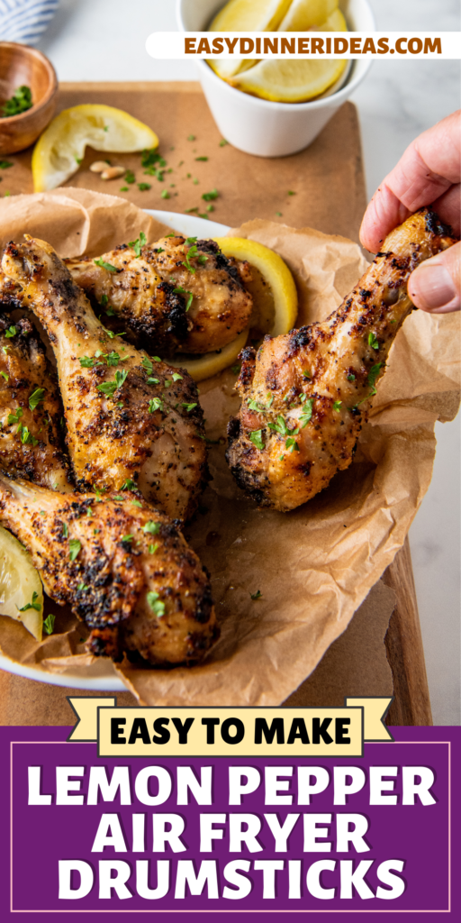 Air Fryer Drumsticks in a basket with parchment paper with a hand picking up one chicken drumstick.