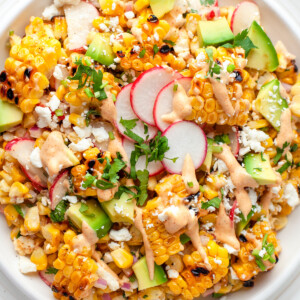 a large plate with Mexican Corn Salad that has corn, radishes, herbs, cheese, and creamy dressing
