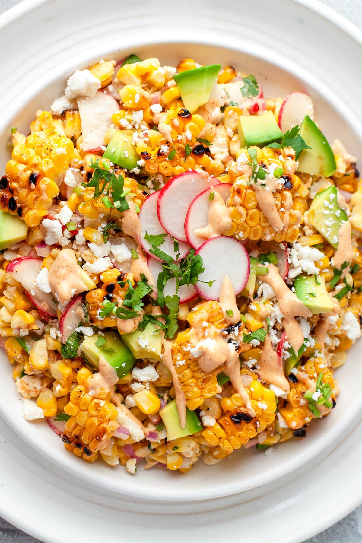 a large plate with Mexican Corn Salad that has corn, radishes, herbs, cheese, and creamy dressing