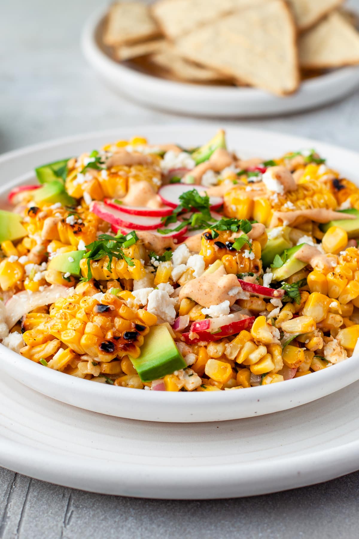 a large plate with Mexican Corn Salad that has corn, radishes, herbs, cheese, and creamy dressing