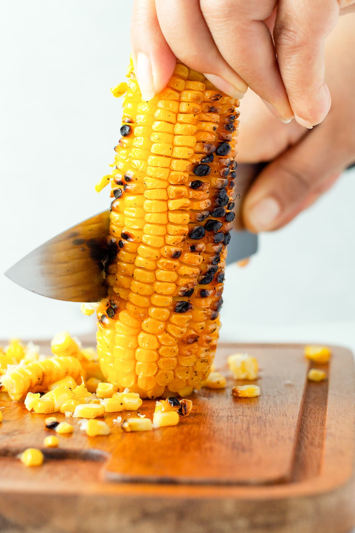 a knife cutting charred corn off the cob