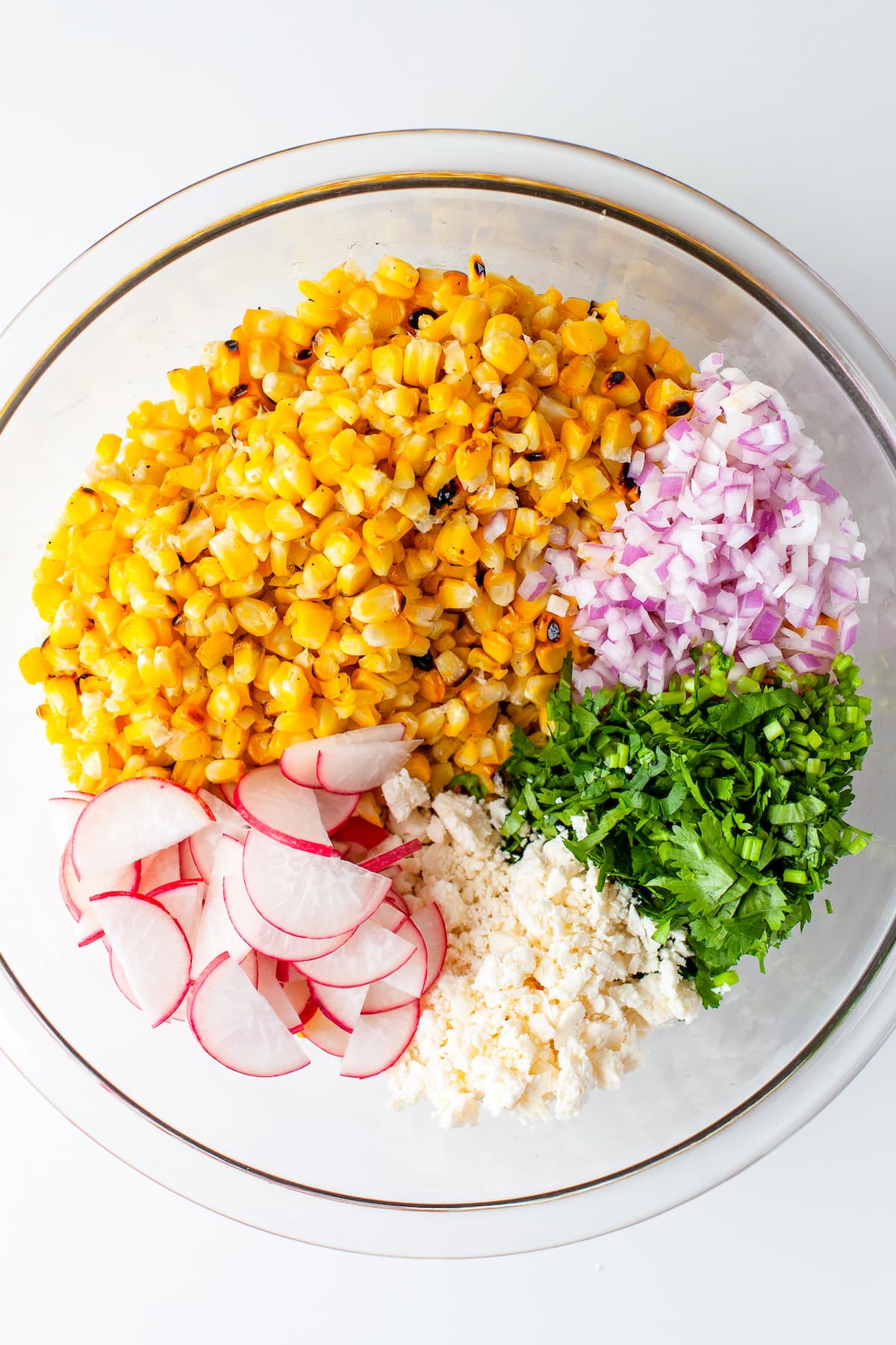 a glass bowl with corn, radishes, cotjia cheese, cilantro, and red onions