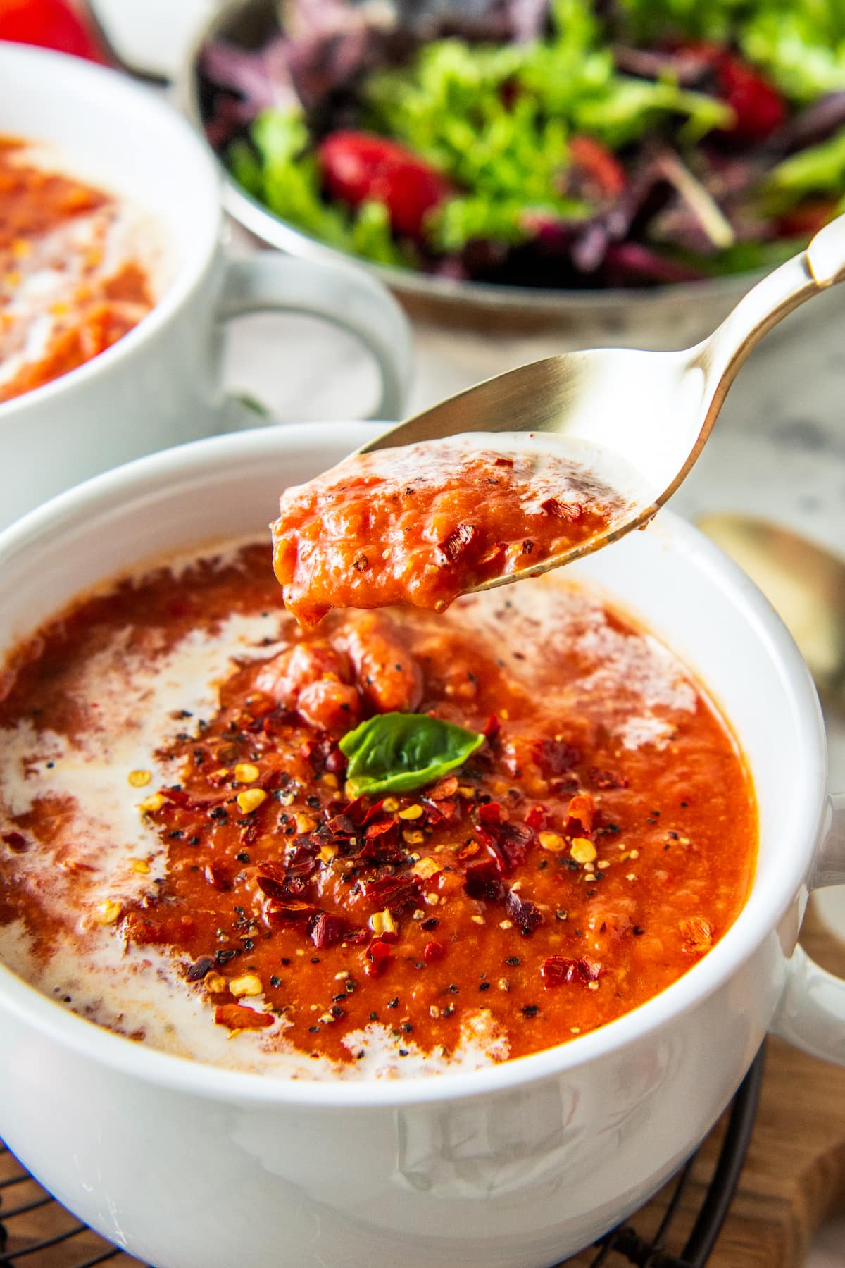 a bowl of roasted tomato soup garnished with cream and basil with a spoon taking a bite out