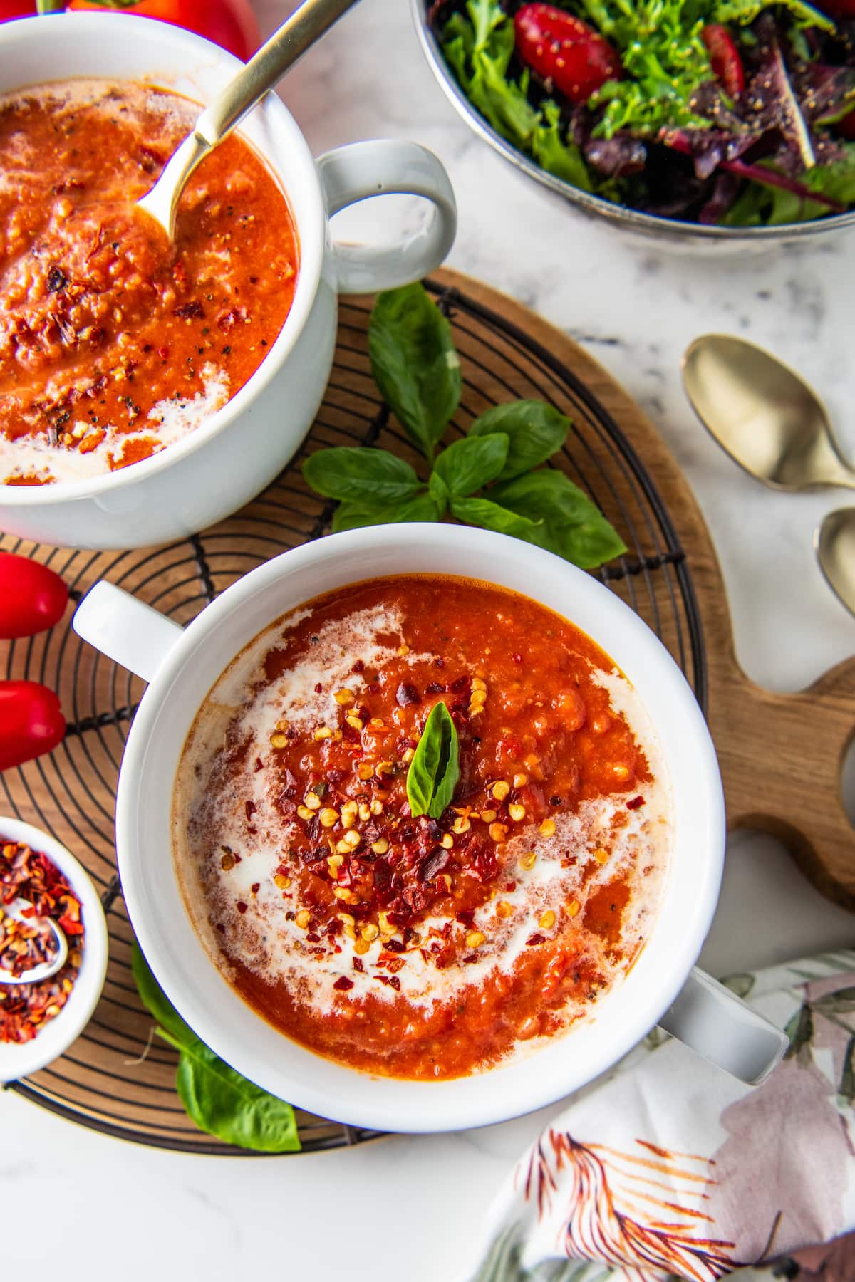 two bowls of roasted tomato soup with fresh basil and chili flakes on the side