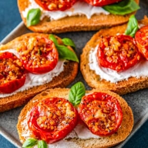 roasted tomatoes on pieces of toast on top of a cream spread