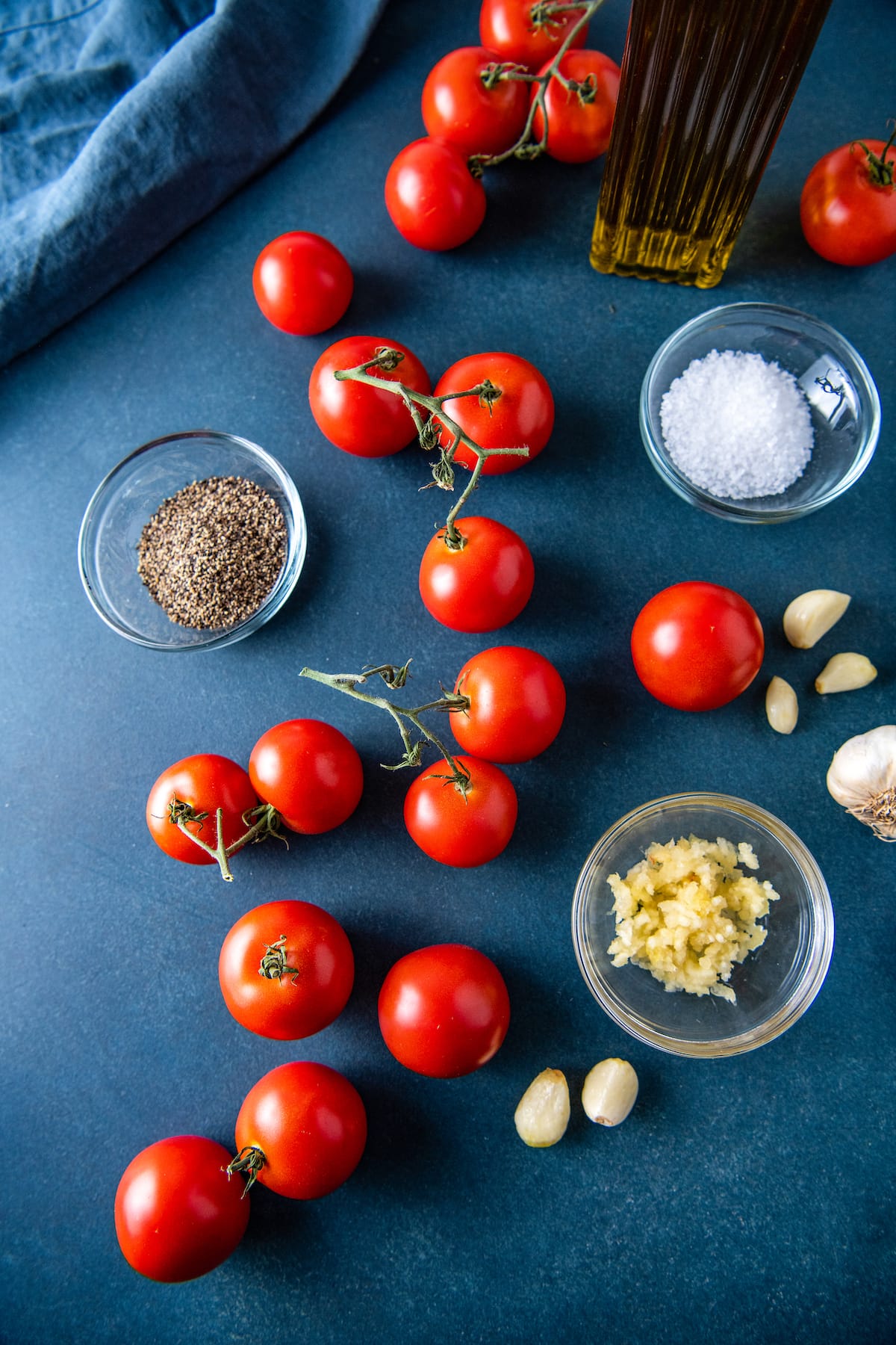 a blue countertop with tomatoes, garlic, salt, and pepper