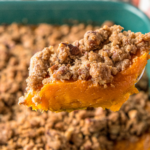 A serving spoon scooping up a serving of sweet potato souffle out of a casserole dish.