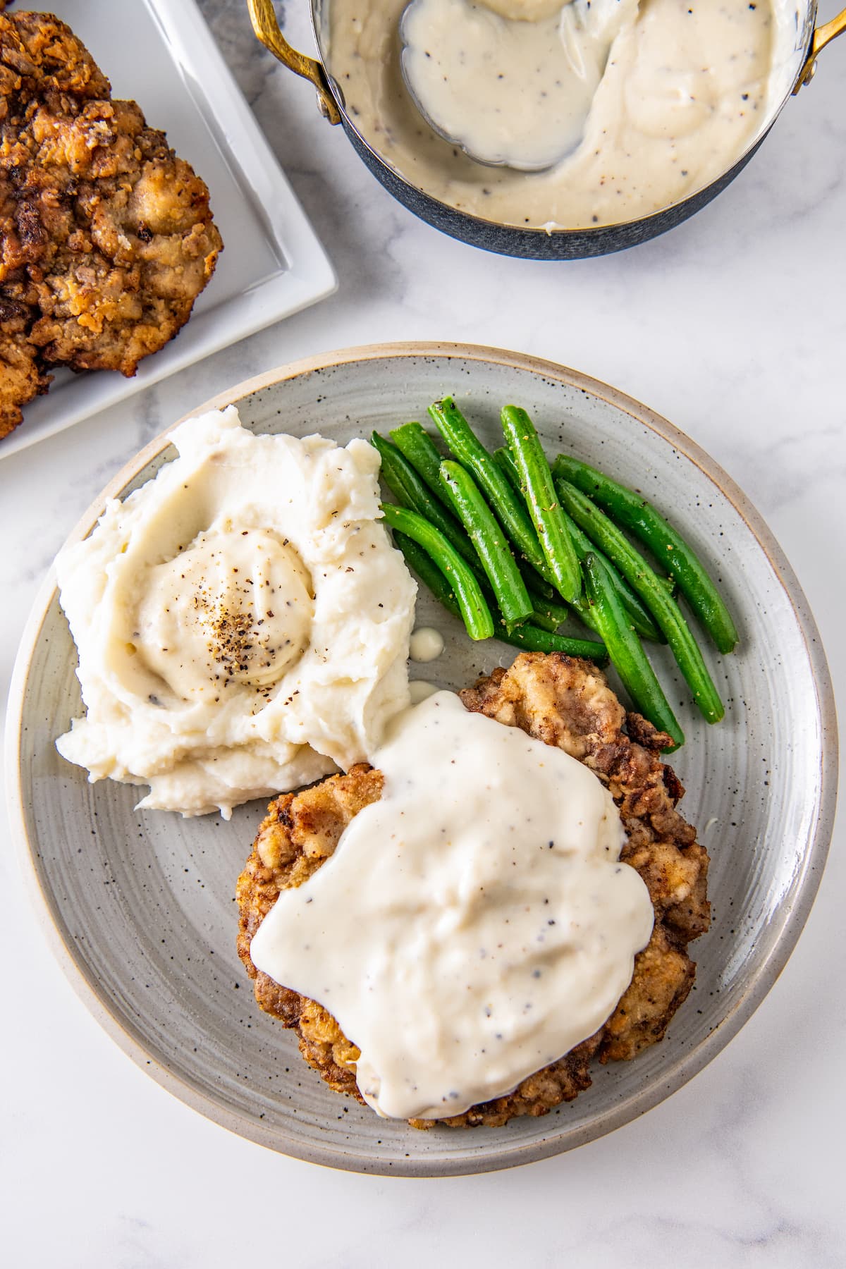 a plate with chicken fried chicken and white gravy next to mashed potatoes and green beans