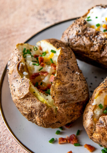 a plate with baked potatoes and cheese, bacon bits, and sour cream
