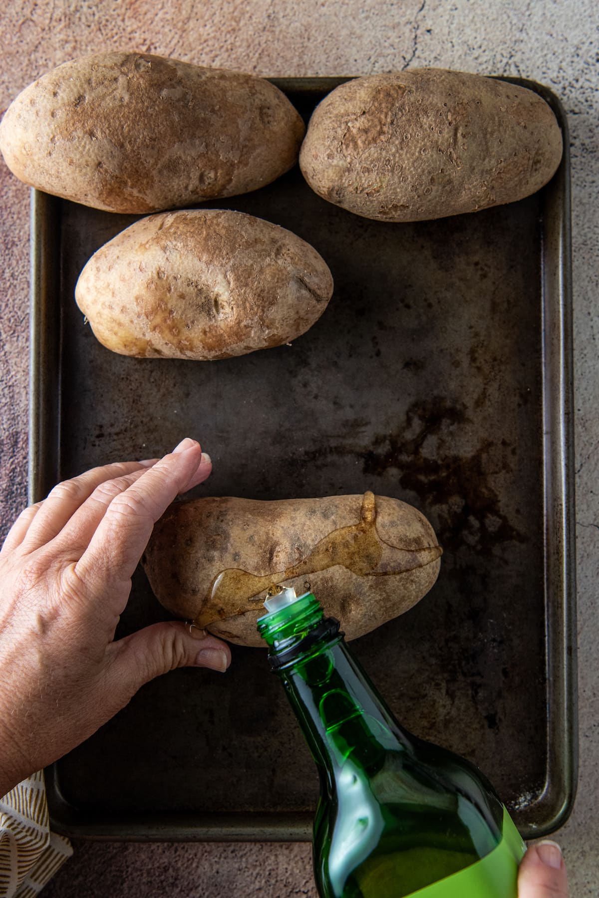 pouring oil on a whole potato on a sheet tray