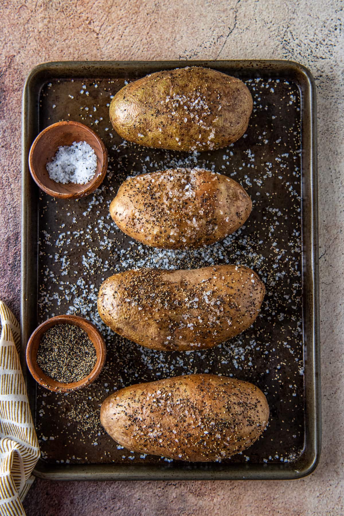 four potatoes on a sheet tray seasoned with salt and pepper