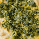 Up close image of a chicken breast with pesto on top in a skillet.