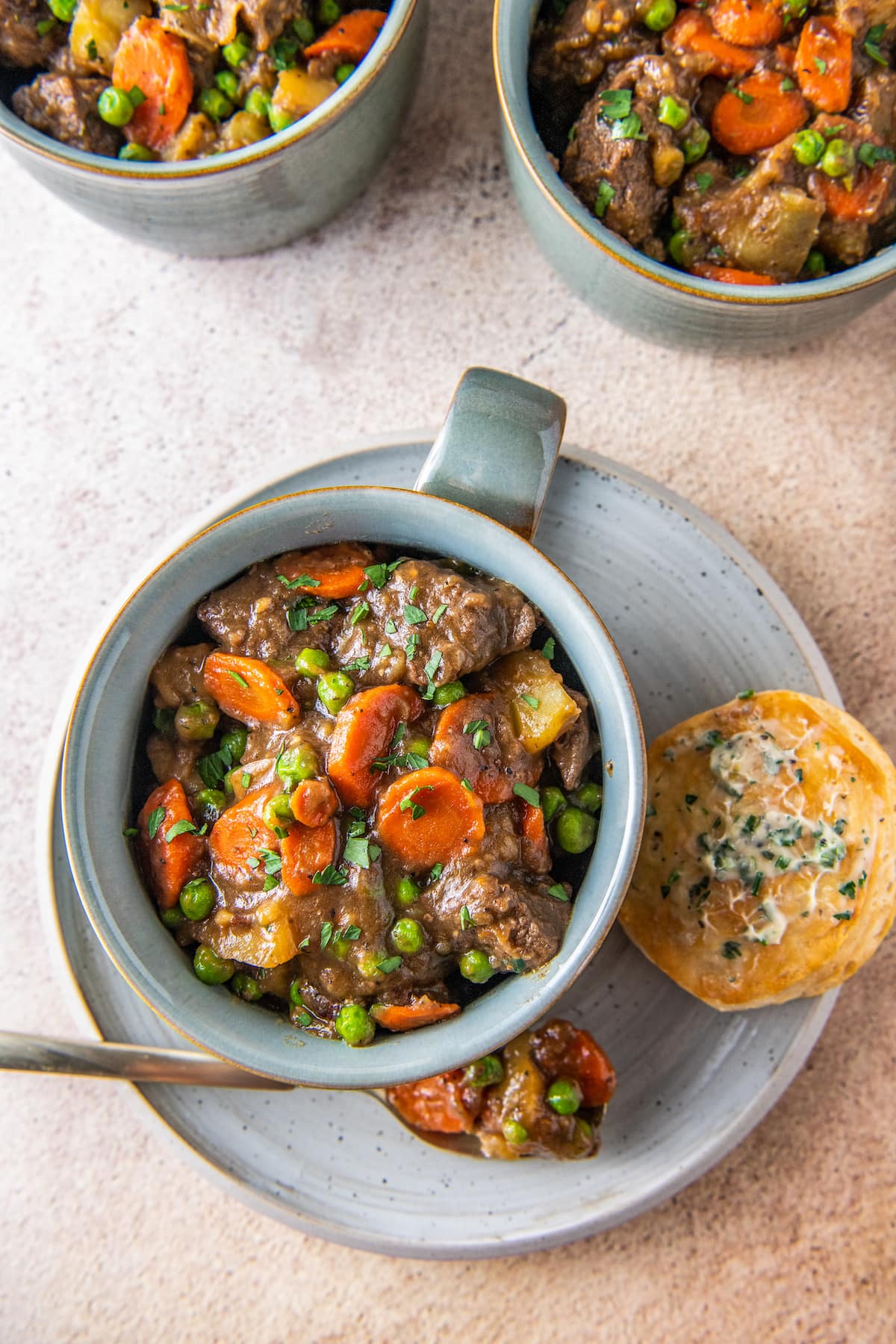 a cup of beef stew on a plate next to some rolls