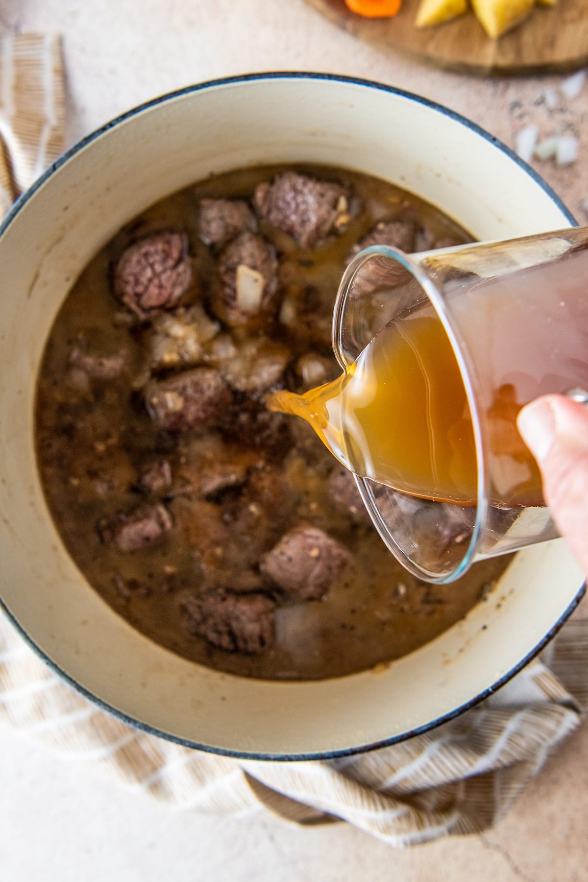 pouring broth into a pan with cooked chunks of beef