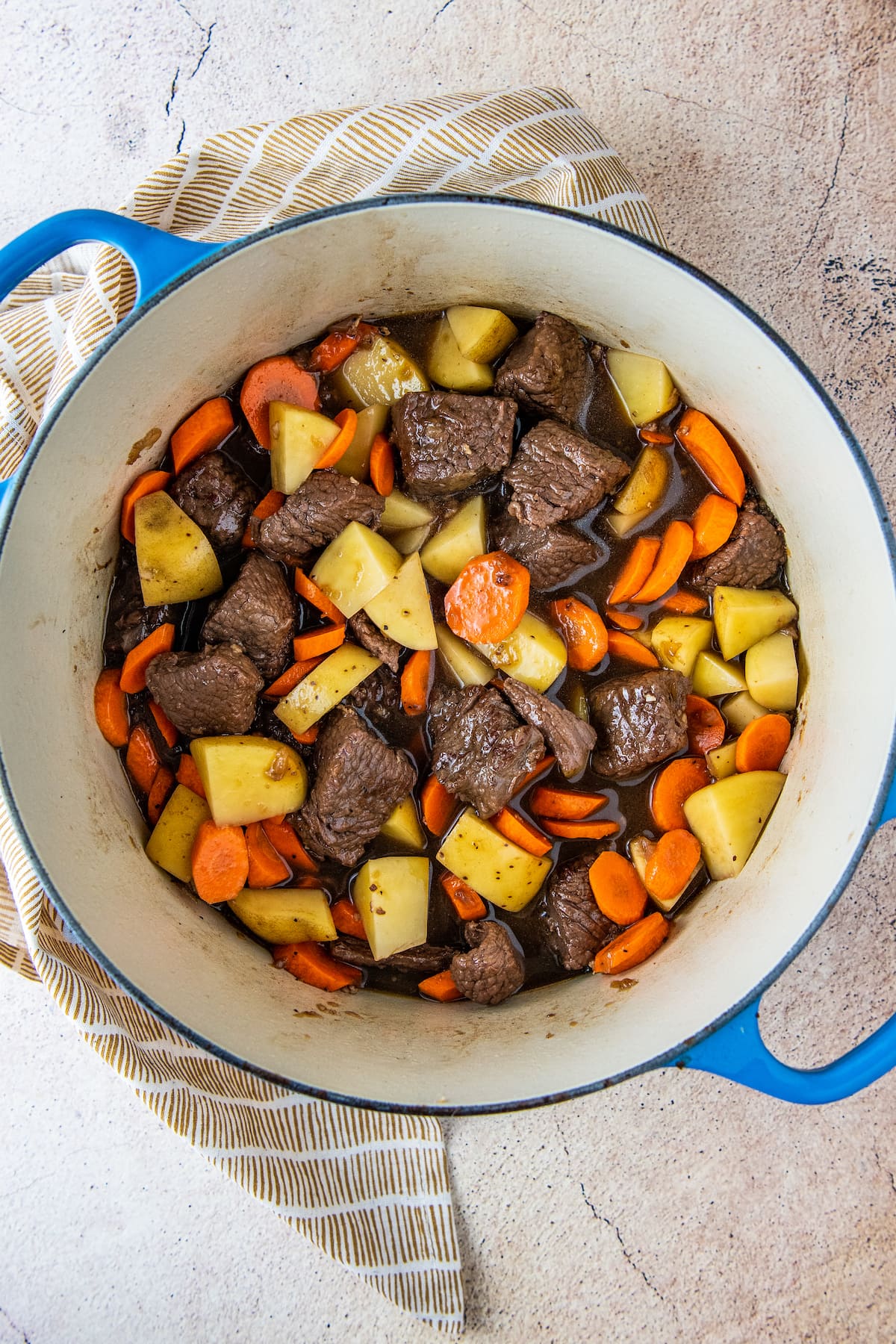 cooked pieces of beef with cut up carrots, onions, and poatoes