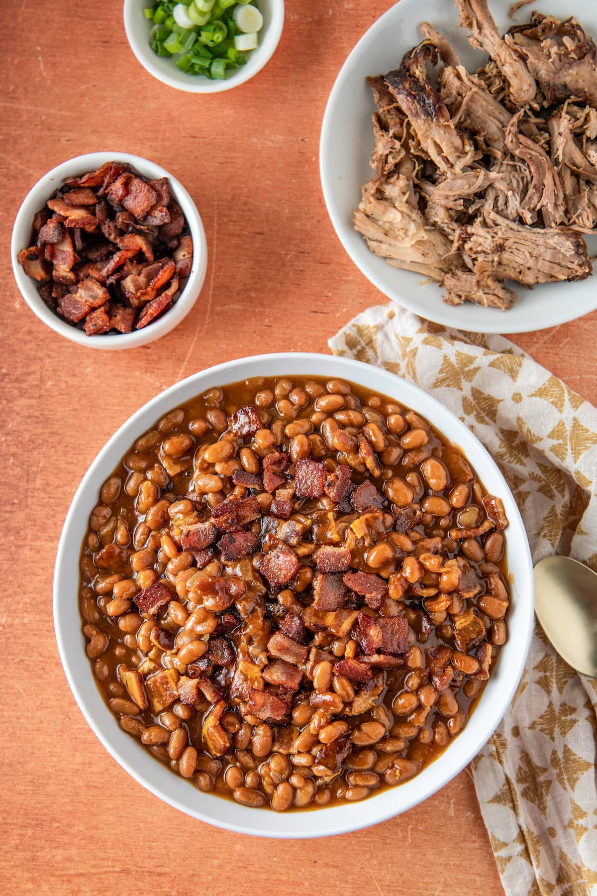 a large bowl of baked beans and two bowls with bacon and pulled pork