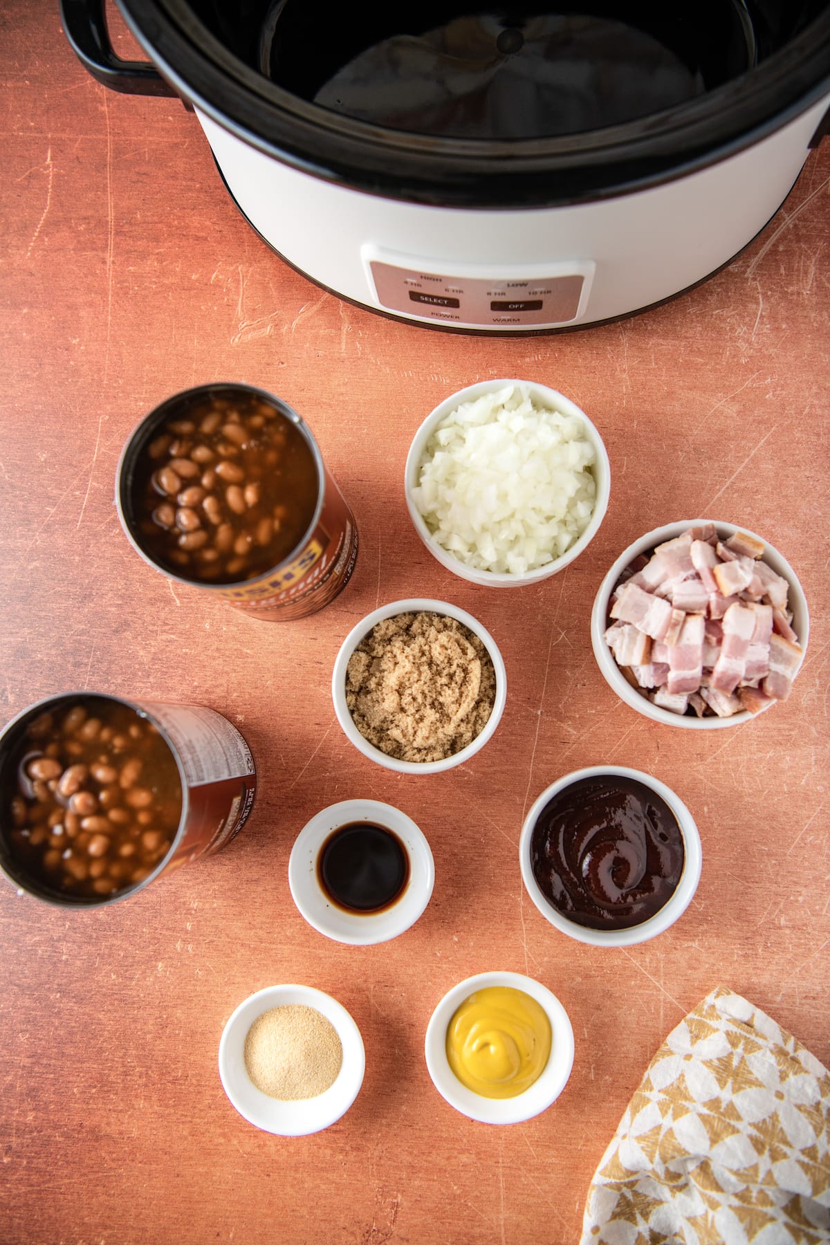ingredients to make baked beans like canned beans, onions, bacon, and seasonings