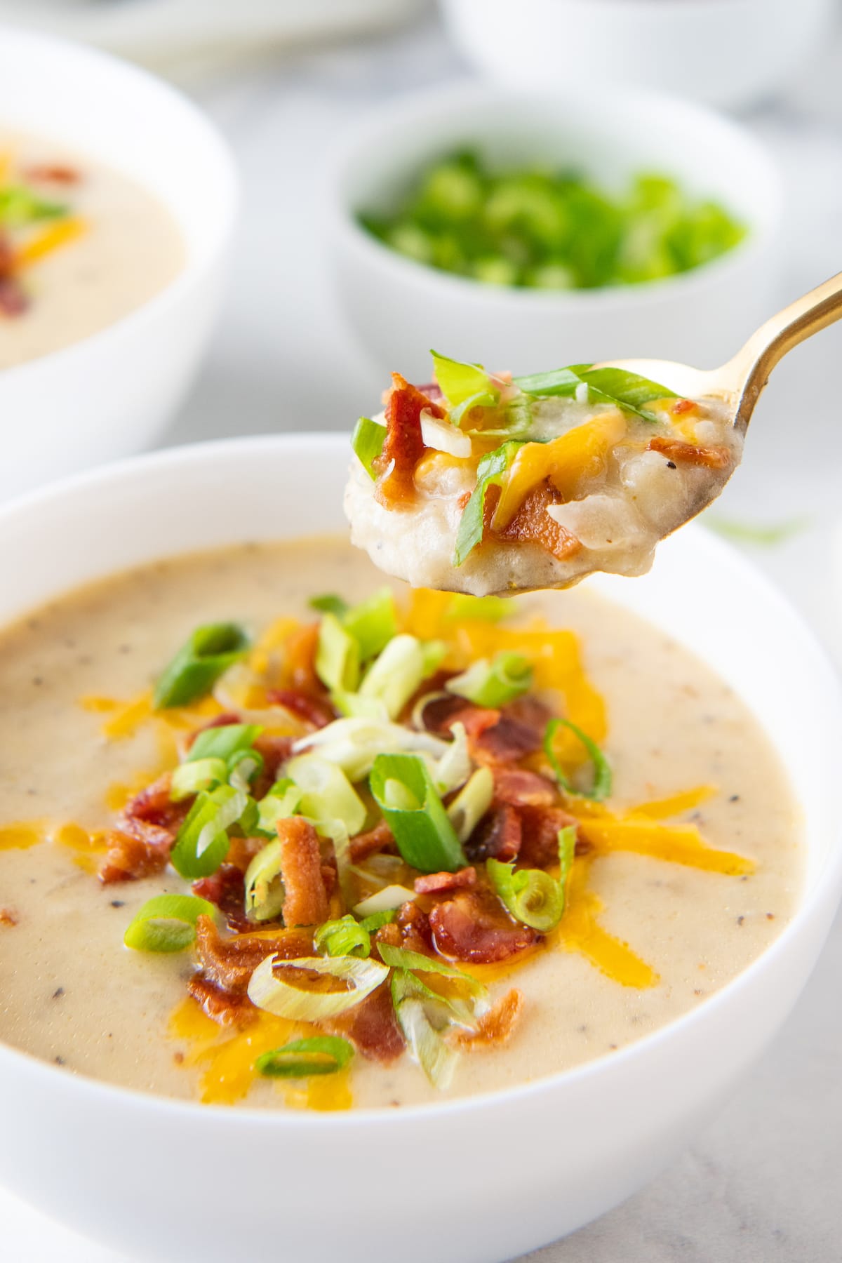 a bowl with baked potato soup and a spoonful taking a bite out