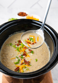 a ladle with crockpot baked potato soup over a slow cooker with soup